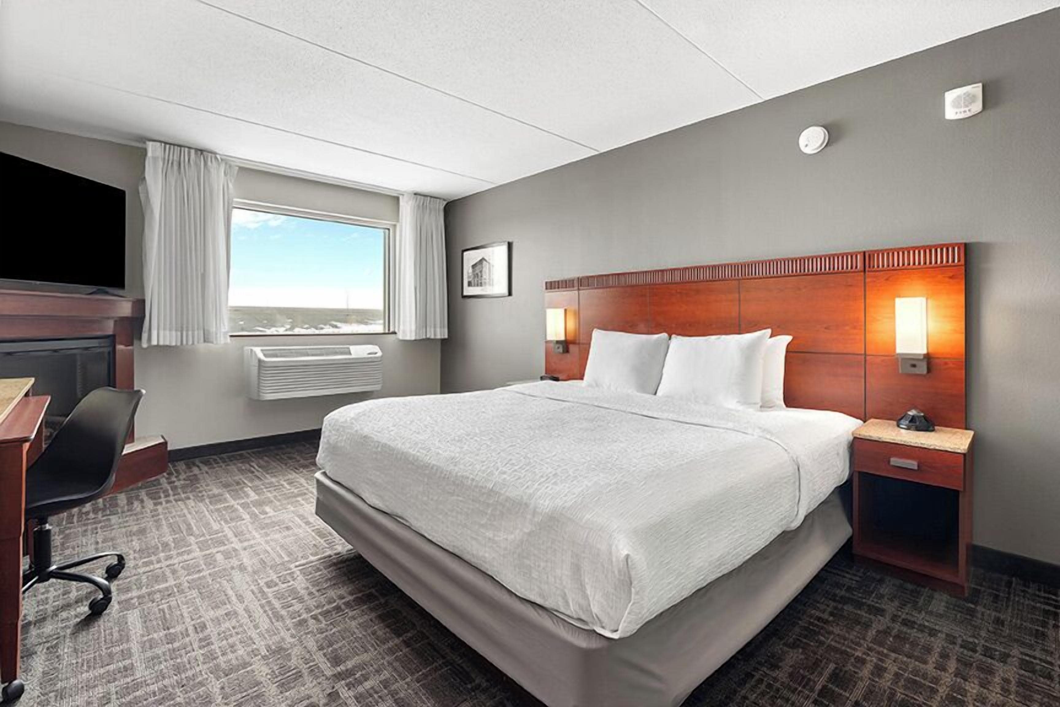 A hotel room with a large bed, a desk with a chair, a TV, a window with curtains, and a nightstand with a lamp.