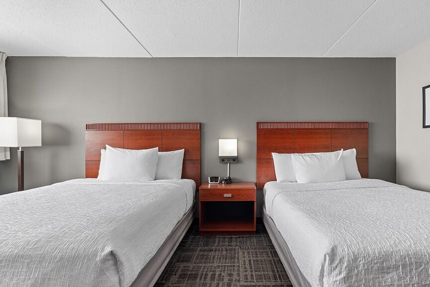 Habitación de hotel con dos camas, una mesita de noche con lámpara y una lámpara de pared.