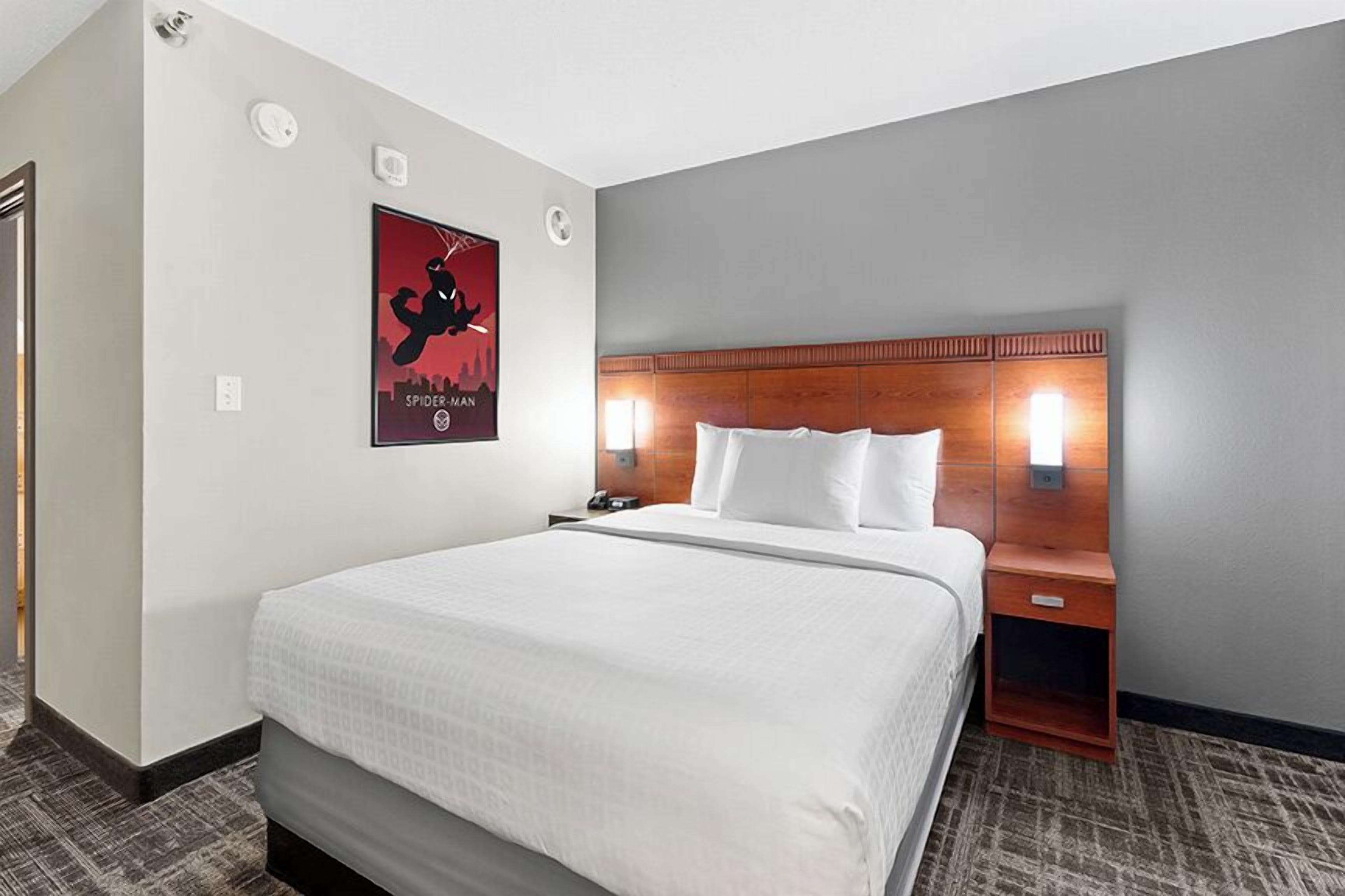 Een hotelkamer met een groot bed, een houten hoofdbord, een nachtkastje en een poster aan de muur.
