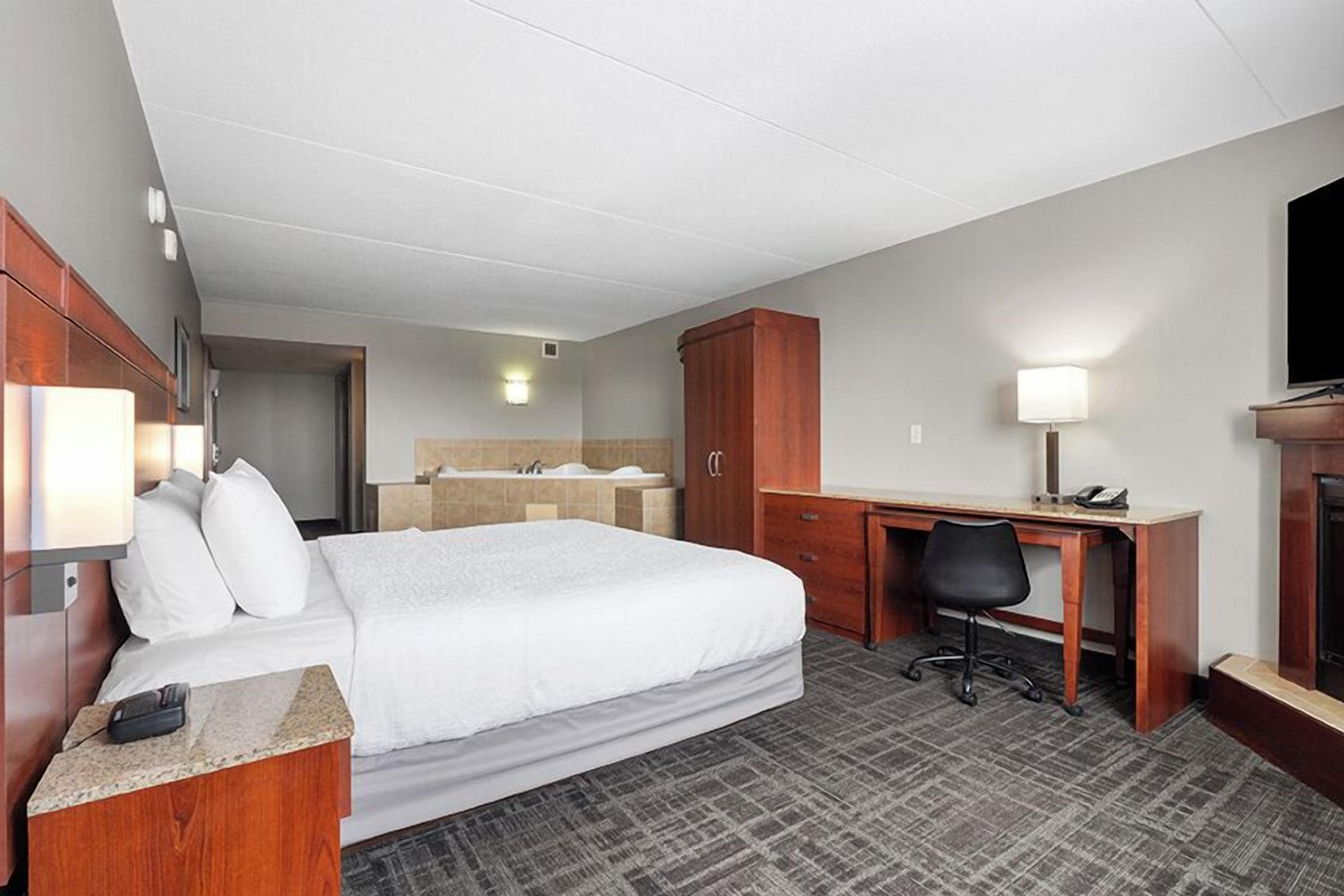 Quarto de hotel com cama, escrivaninha, cadeira e televisão.
