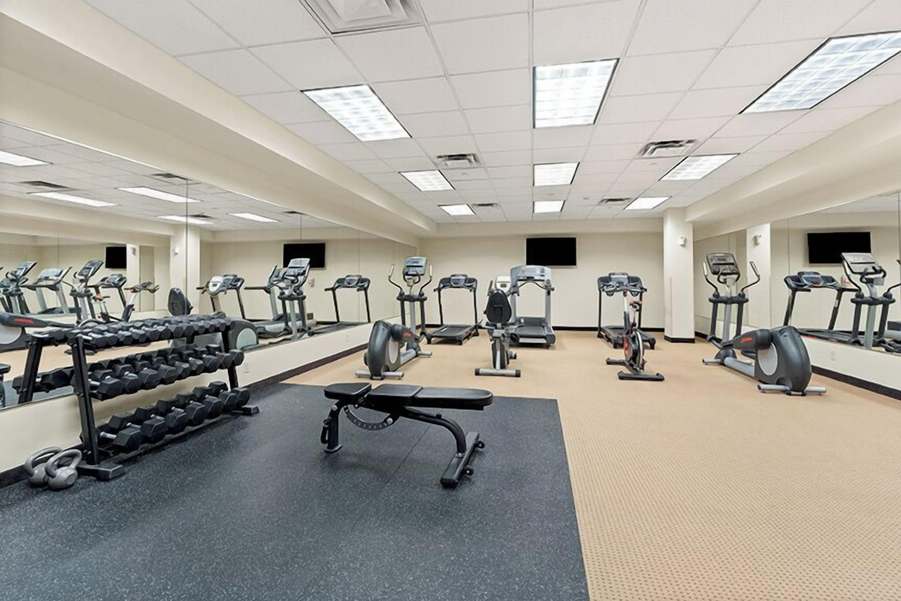 A gym with exercise equipment, mirrors, and a weight rack.