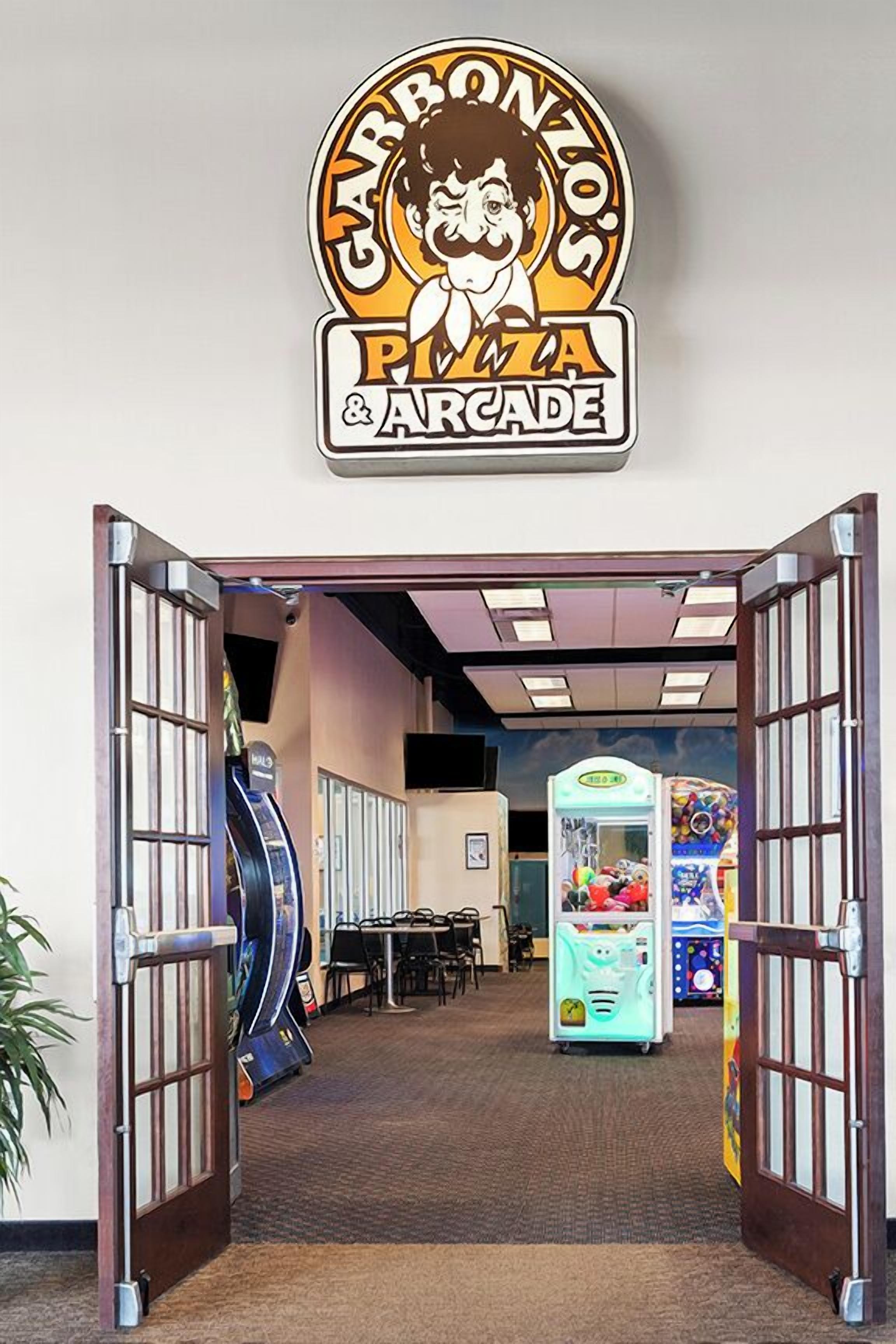 An entrance to a venue with a sign for 'Carbonzo's Pizza & Arcade,' featuring arcade machines and a pizza vending machine.