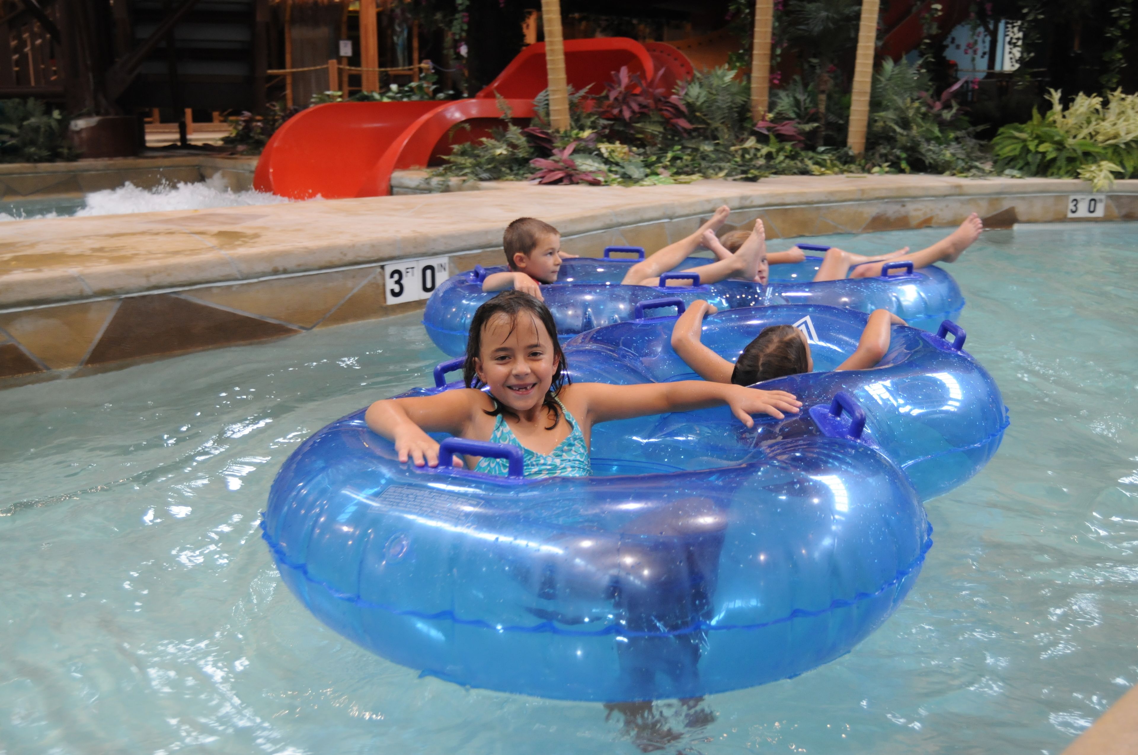 A pool area with inflatable tubes, a water slide, and a plant-lined walkway.