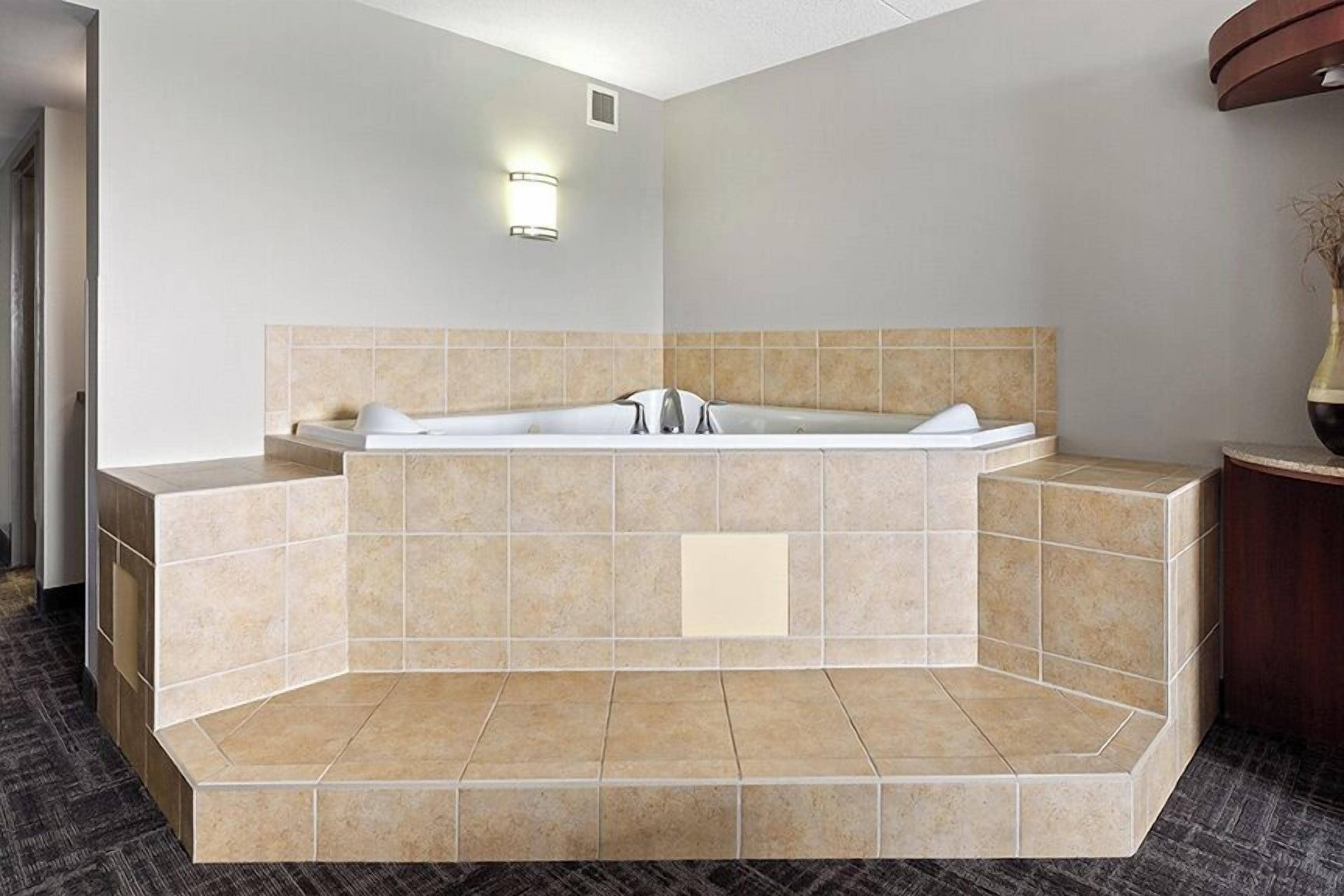 A modern bathroom with a freestanding bathtub, a wall-mounted light, and a vase on a wooden side table.
