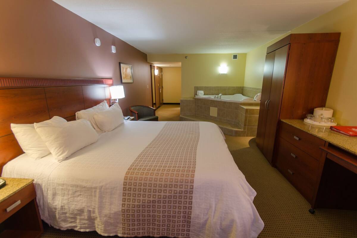 A hotel room with a large bed, a desk, a chair, a bathroom with a bathtub, and a wardrobe.