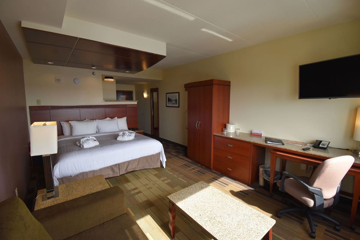 A hotel room with a bed, desk, chair, television, and a wardrobe.