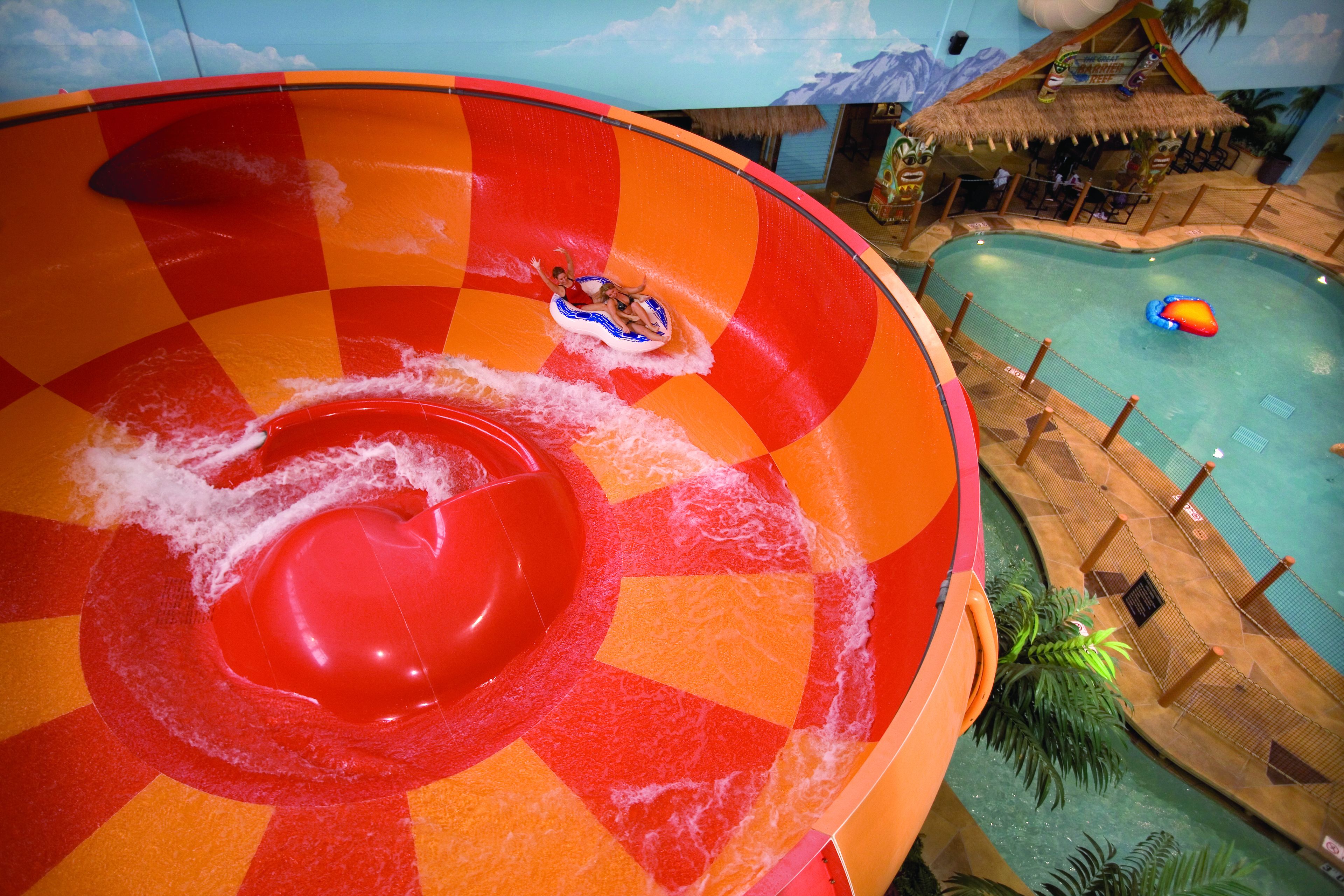 A water slide with a checkered pattern, a pool area with a thatched-roof hut, and a lifeguard stand.