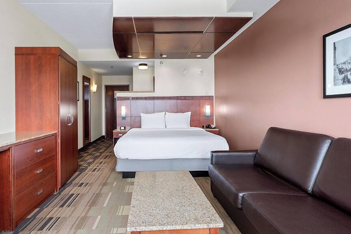 A hotel room with a bed, a sofa, a wooden wardrobe, and a framed picture on the wall.