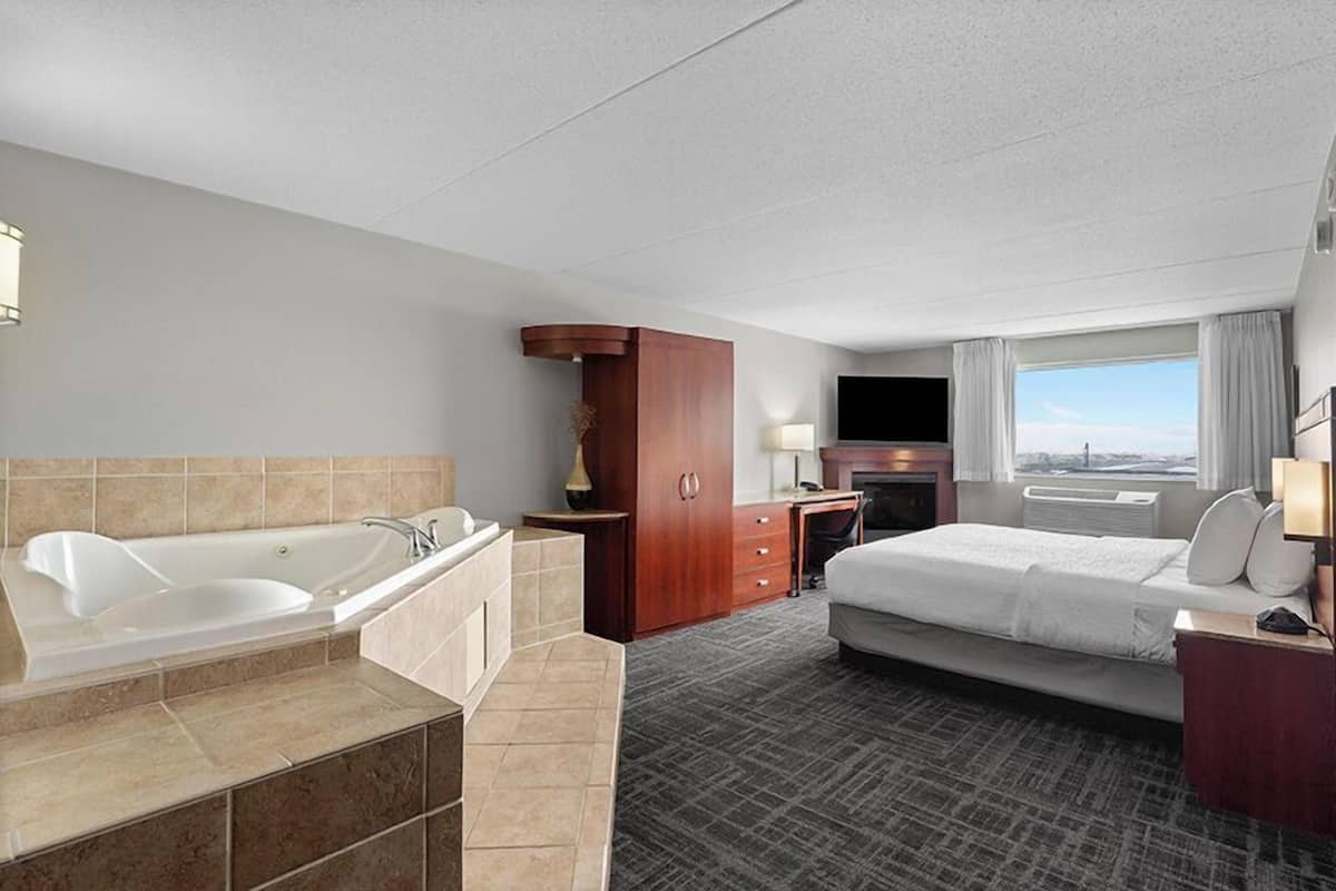 A hotel room with a bathtub, a bed, a desk, and a window with a view.