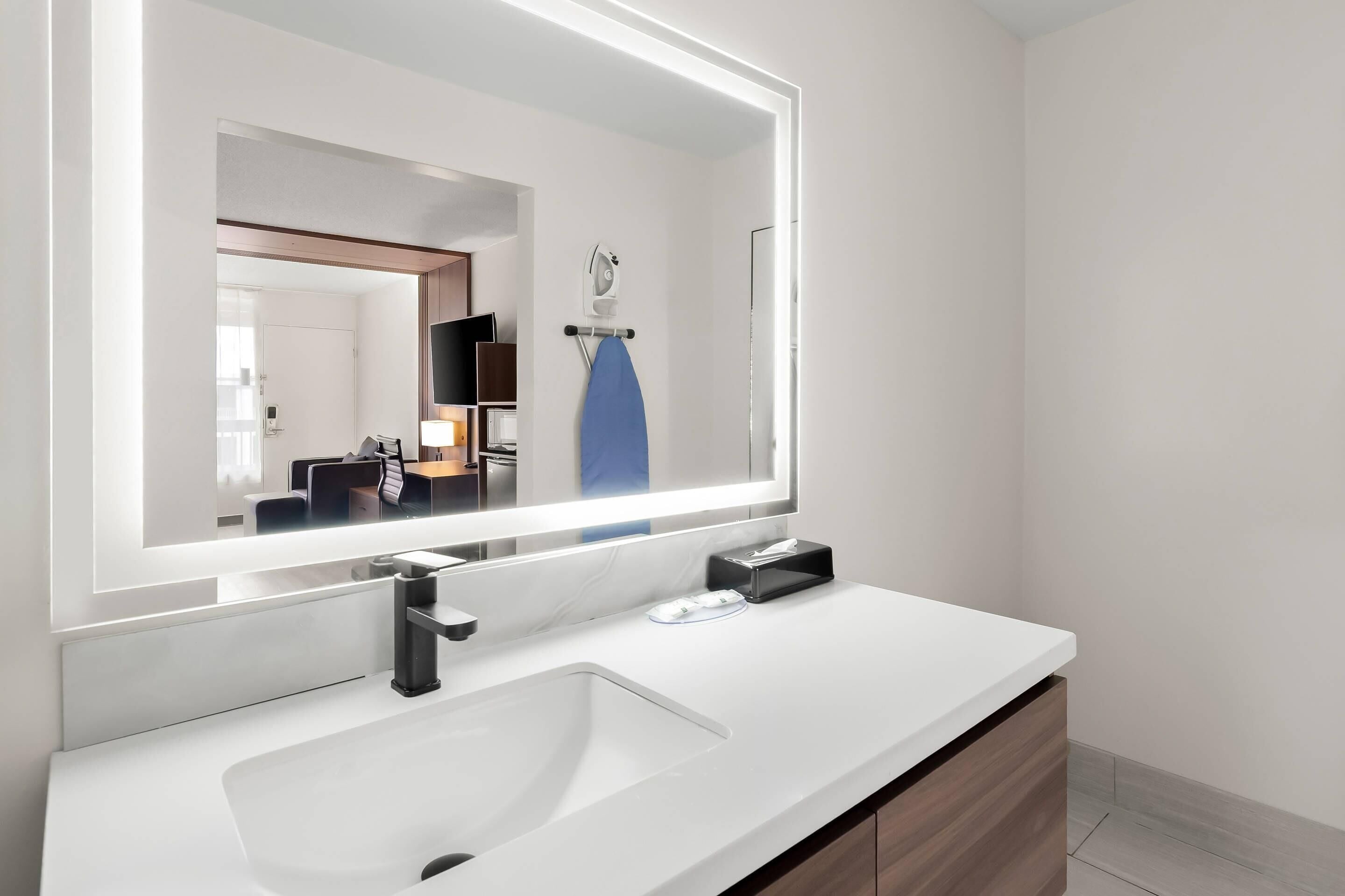 A modern bathroom with a large mirror, white sink, and wooden vanity.