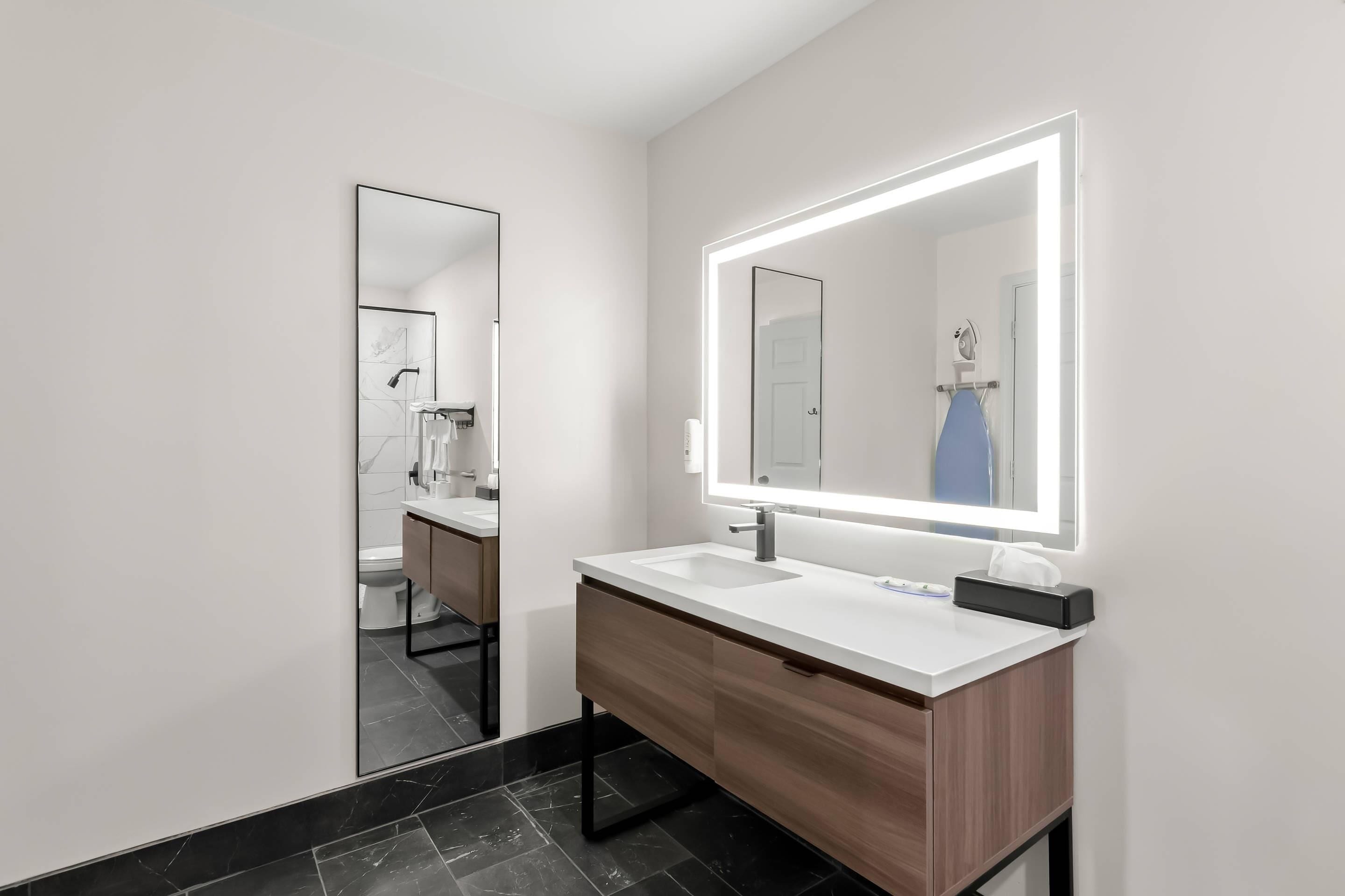 A modern bathroom with a large mirror, white countertop, and dark tiled floor.