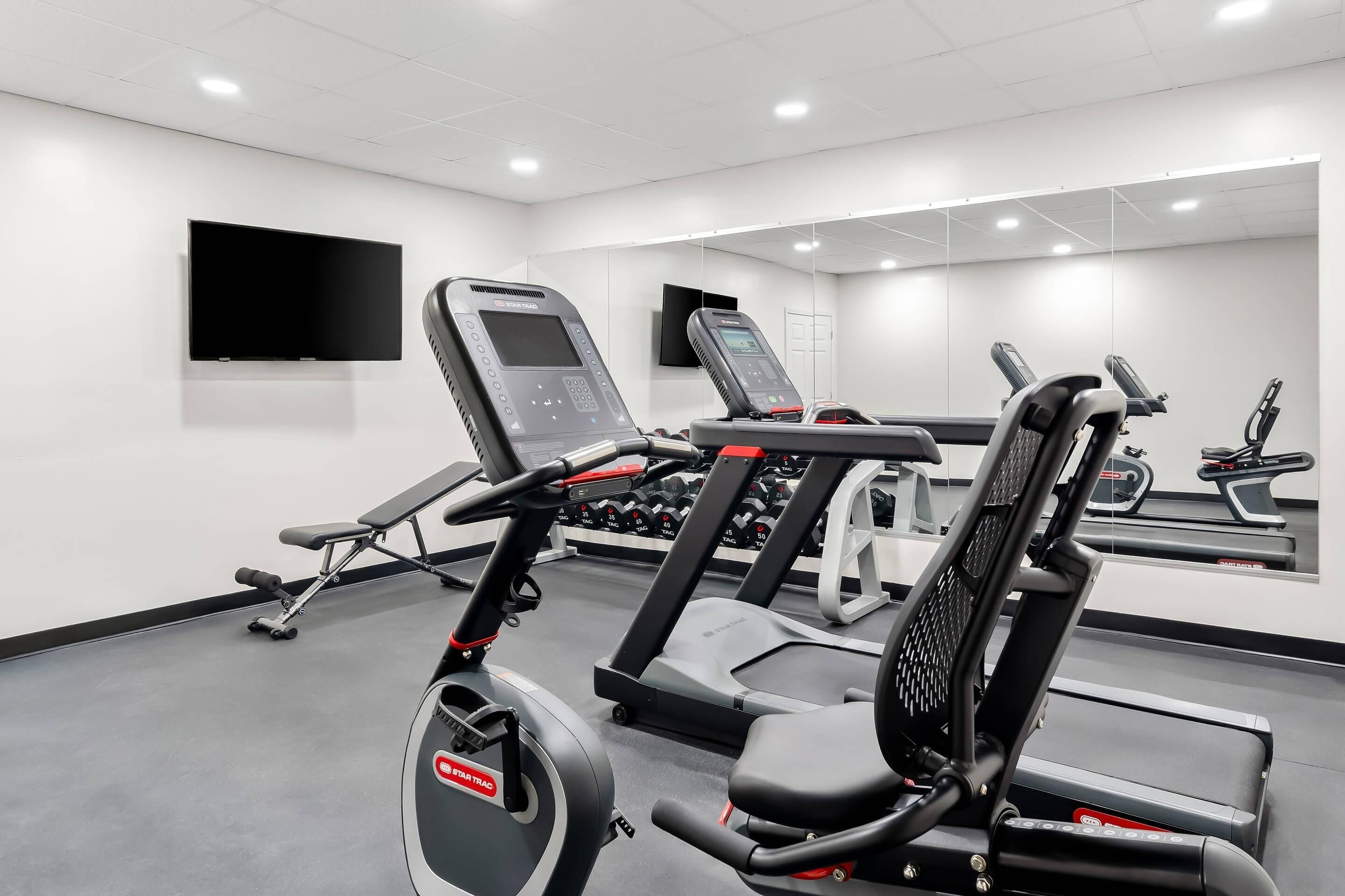Un gimnasio moderno con equipo de cardio, máquinas de pesas y un espejo grande.