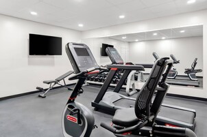 Un gimnasio moderno con equipo de cardio, máquinas de pesas y un espejo grande.