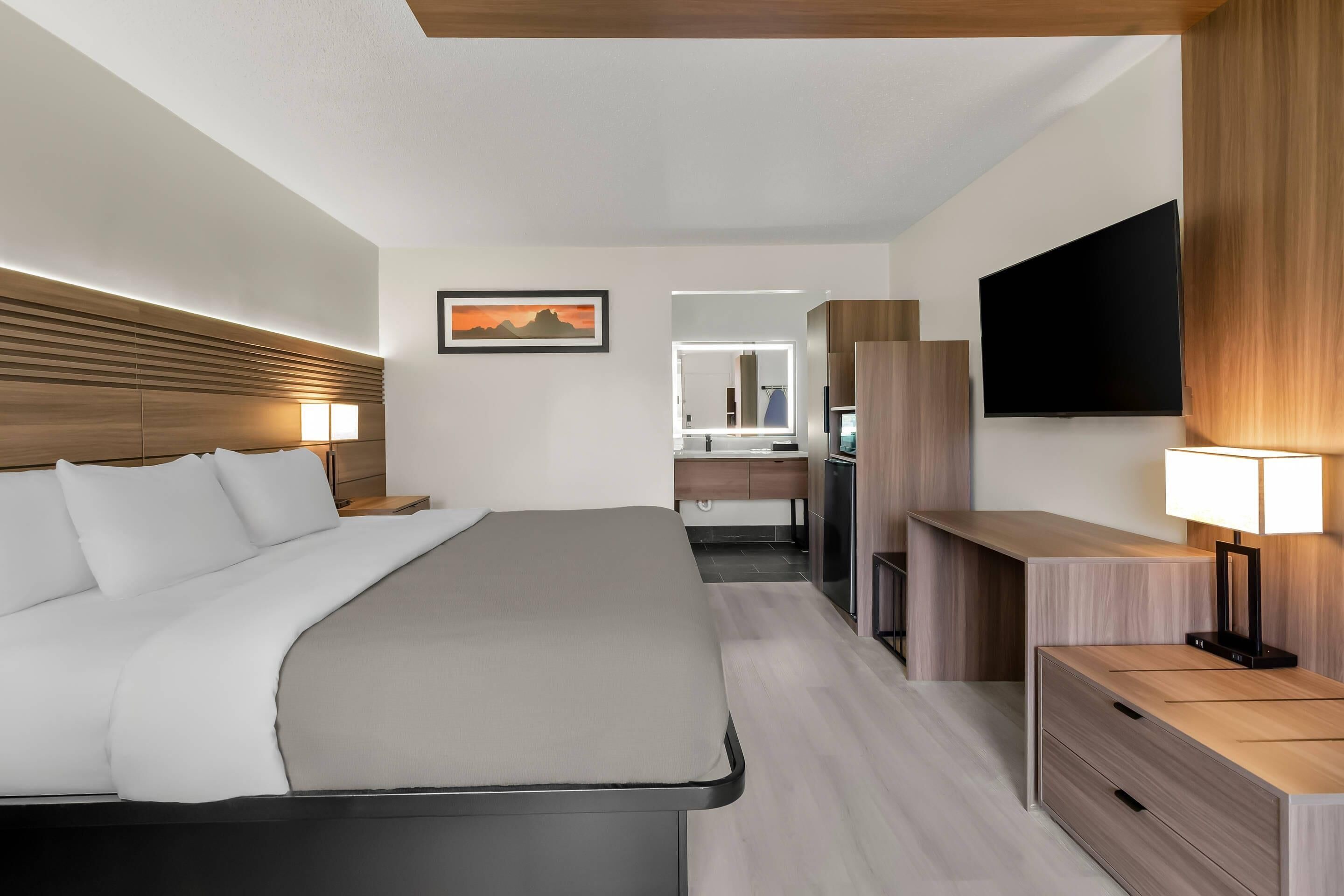 Een moderne hotelkamer met een groot bed, nachtkastjes, een televisie en een badkamer die door een open deur zichtbaar is.