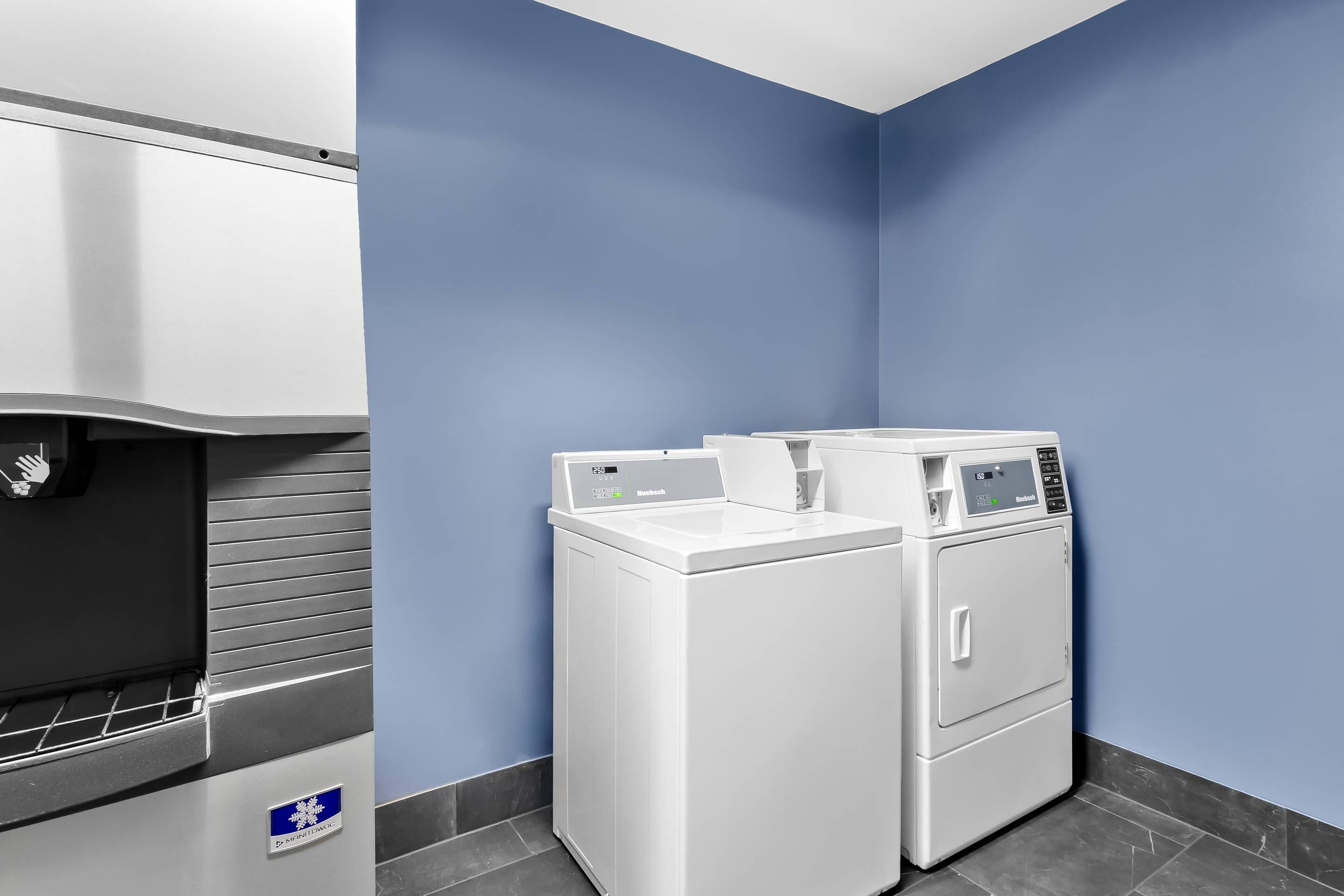 Un cuarto de lavandería con dispensador de agua, dos lavadoras apiladas y una pared azul.
