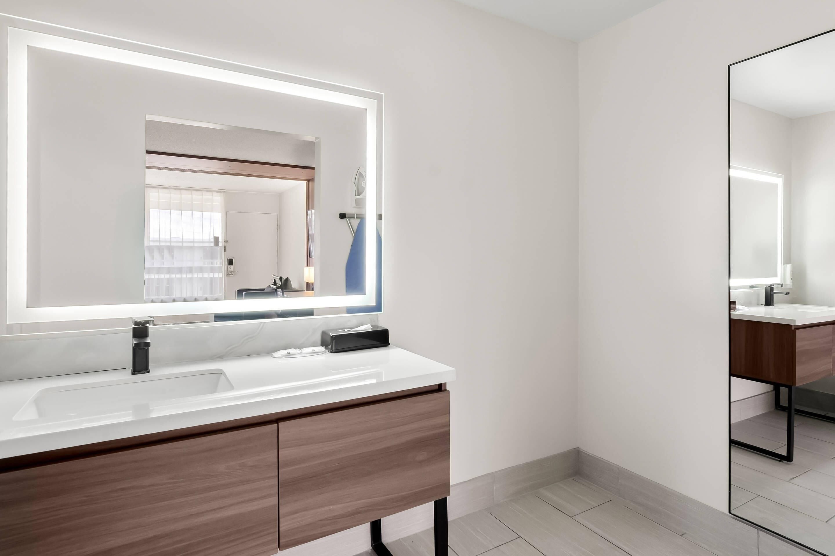 A modern bathroom with a large mirror, white vanity, and a wooden cabinet.