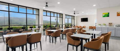 A spacious dining area with tables and chairs, large windows offering a view of the landscape, and a ceiling fan.