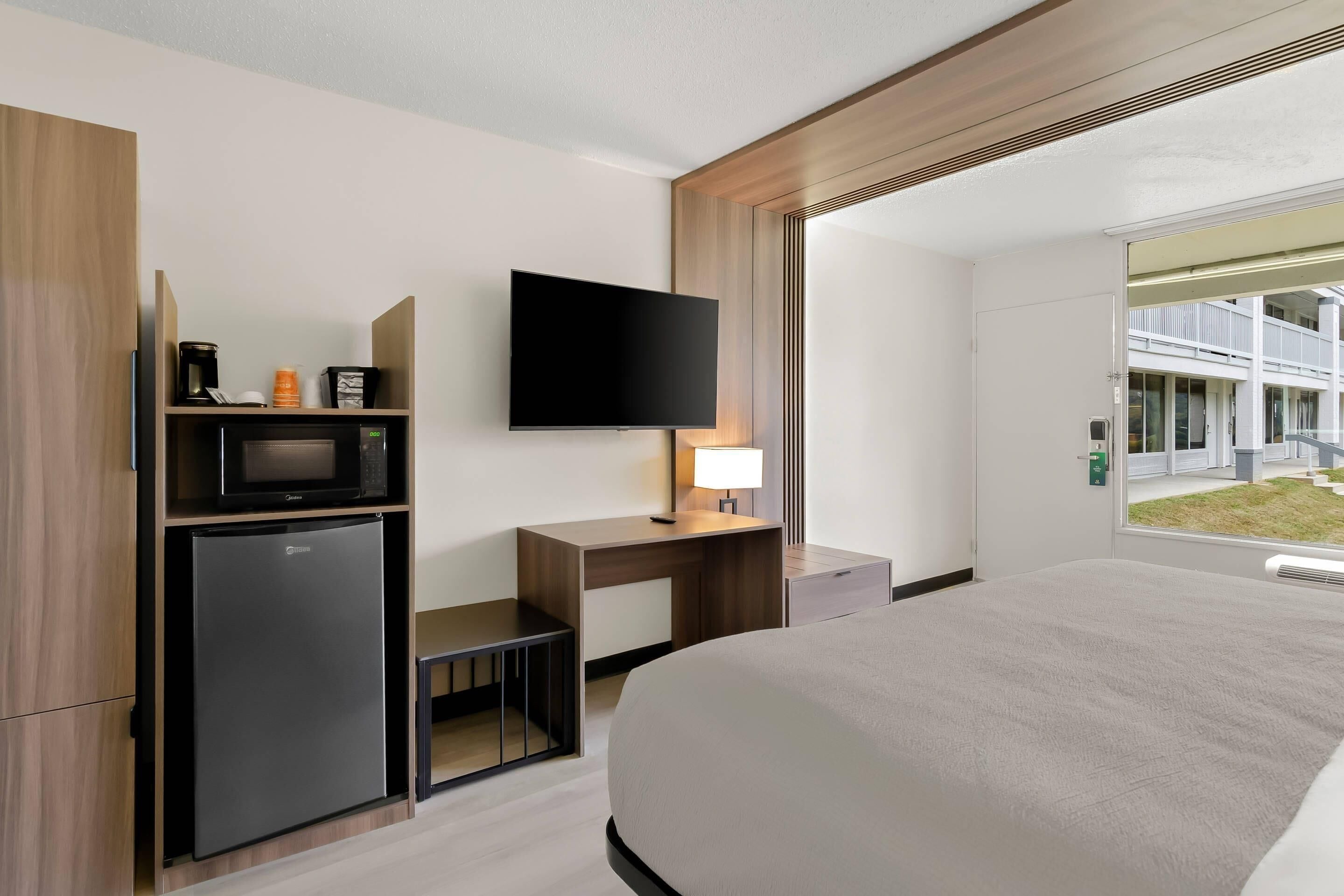 A modern hotel room with a bed, a desk with a flat-screen TV, a microwave, and a refrigerator.