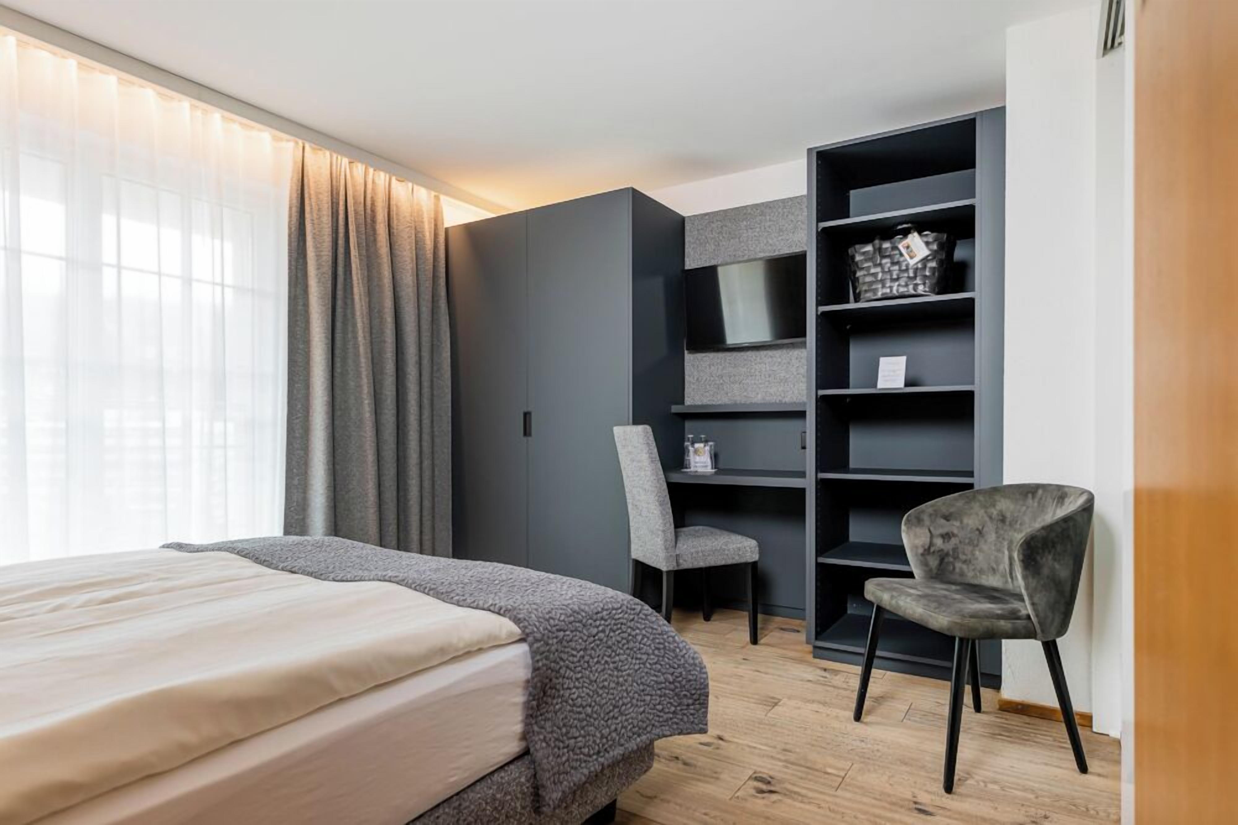 A bedroom with a bed, a chair, a TV shelf, and a wardrobe.