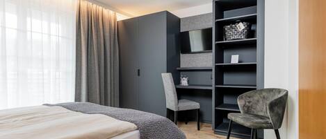 A bedroom with a bed, a chair, a TV shelf, and a wardrobe.