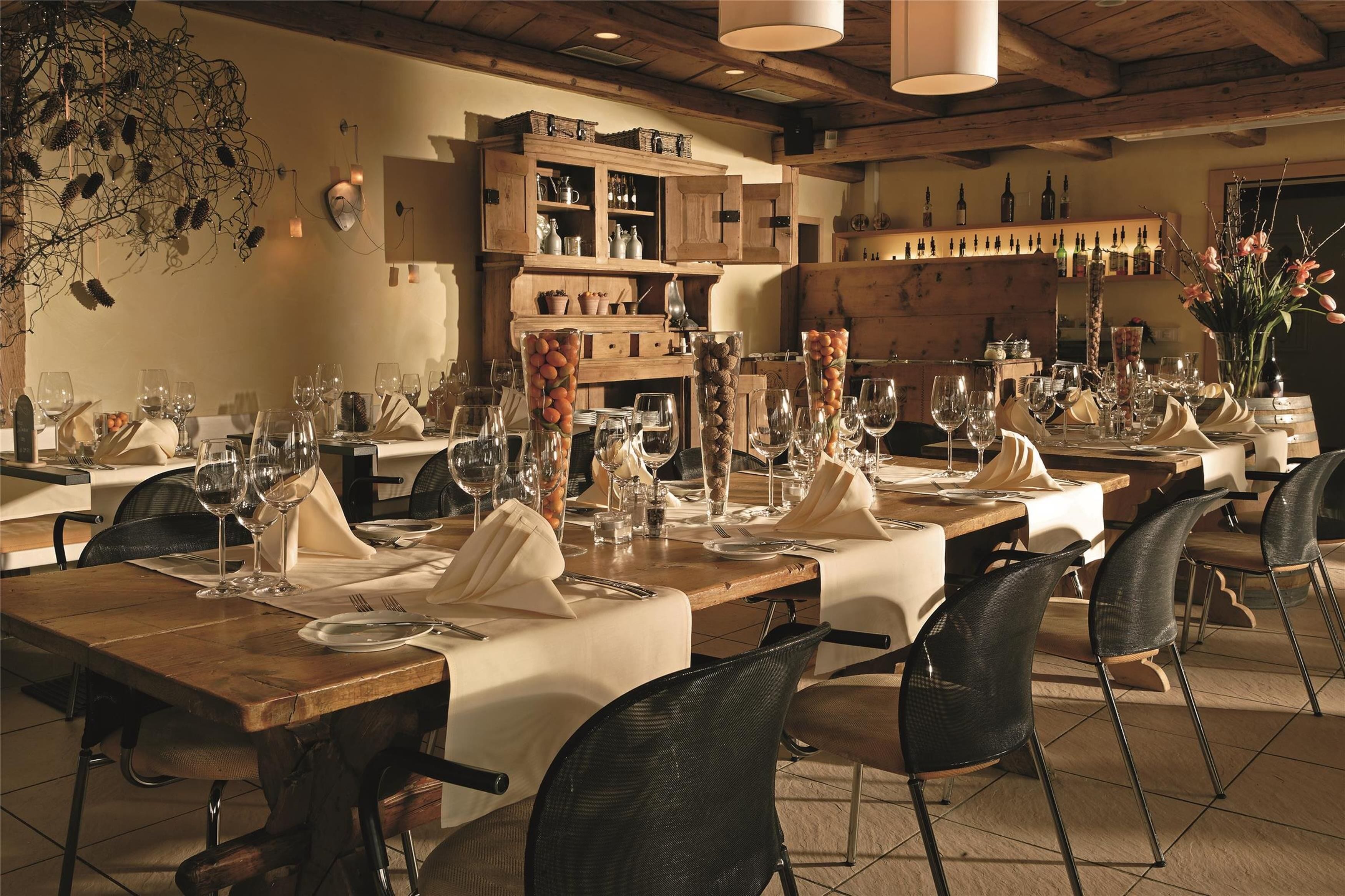 Un restaurant avec des tables en bois, dressées pour le service, agrémentées de nappes blanches et de chaises noires.