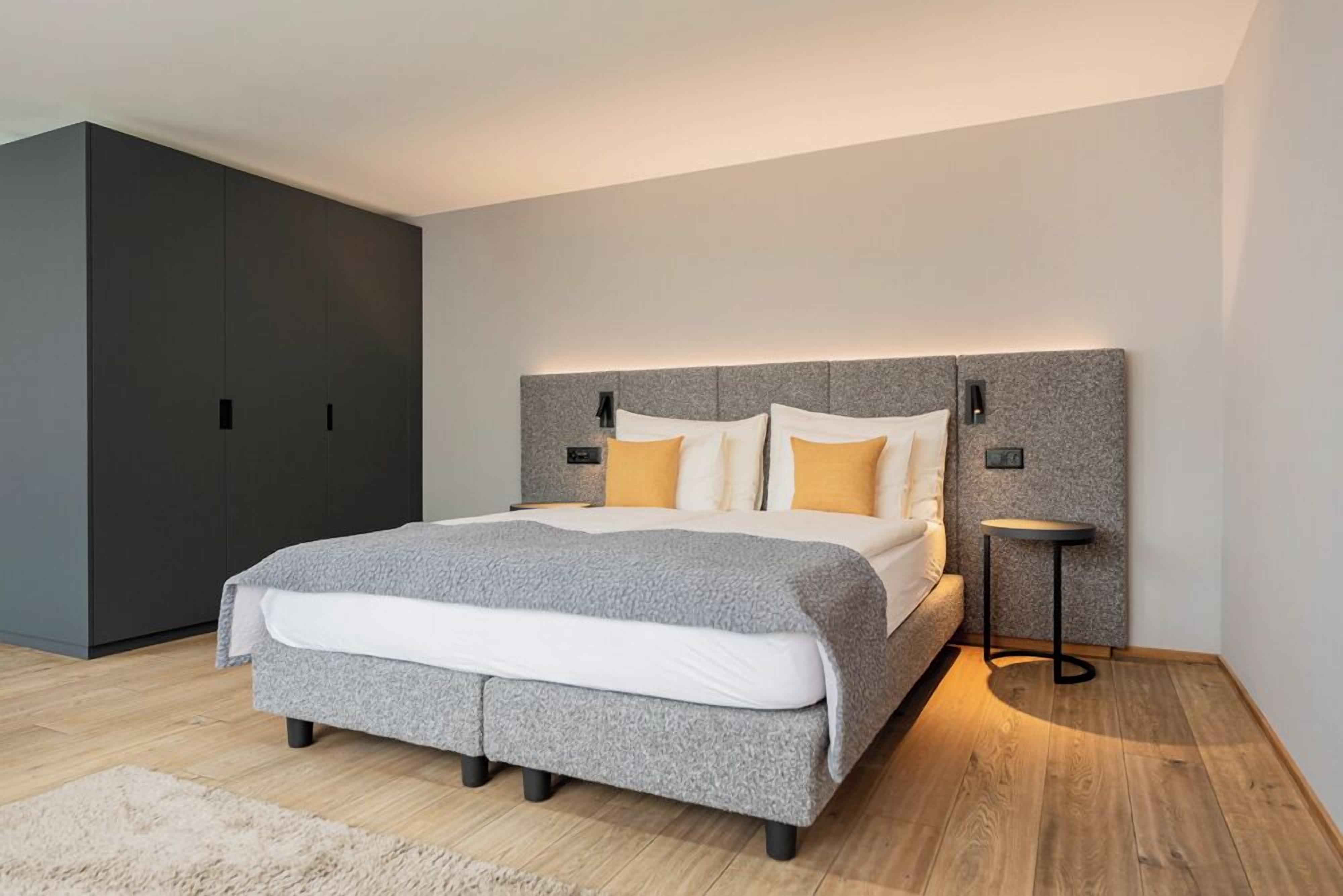 Une chambre à coucher moderne avec un grand lit, une tête de lit grise et une petite table de chevet.