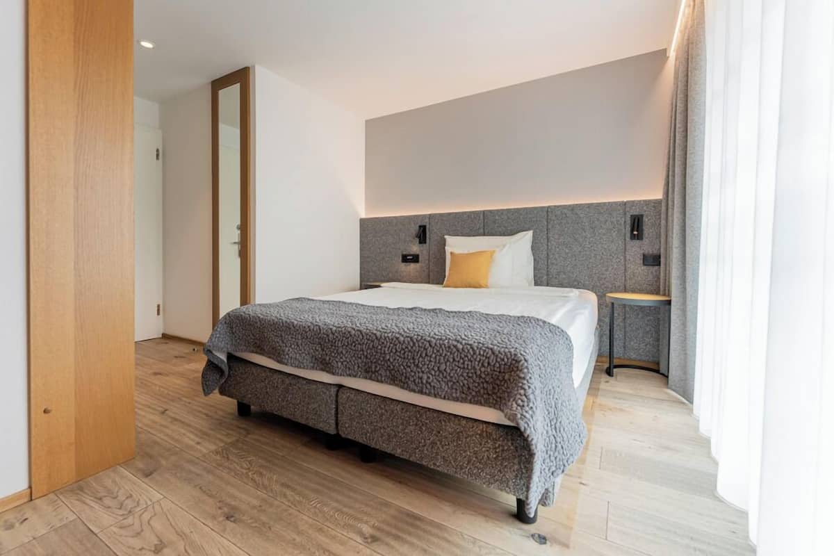 Una habitación de hotel moderna con una cama grande, una mesita de noche, un espejo y piso de madera.