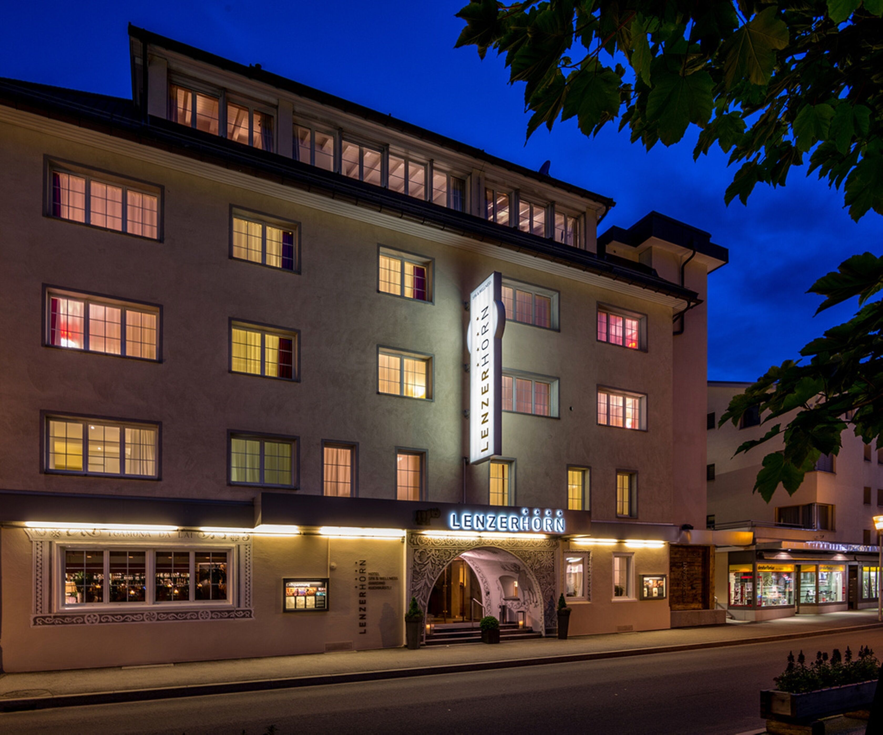 Een meerlaags hotel met een opvallend 'LENZERHORN' bord, met een klassieke architectuur, een centrale ingang en meerdere ramen.