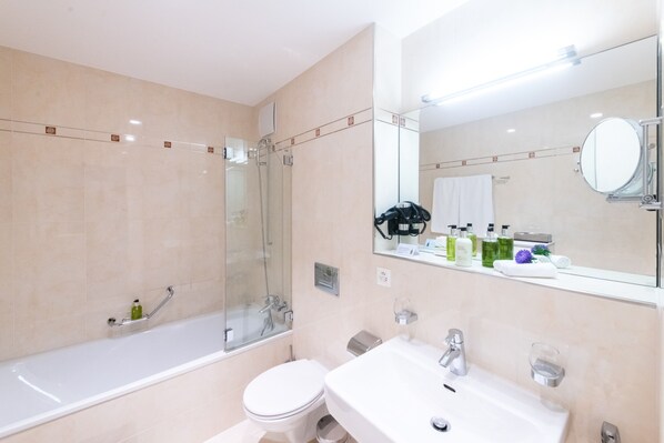 Un baño moderno con ducha de vidrio, inodoro blanco y lavamanos con espejo.