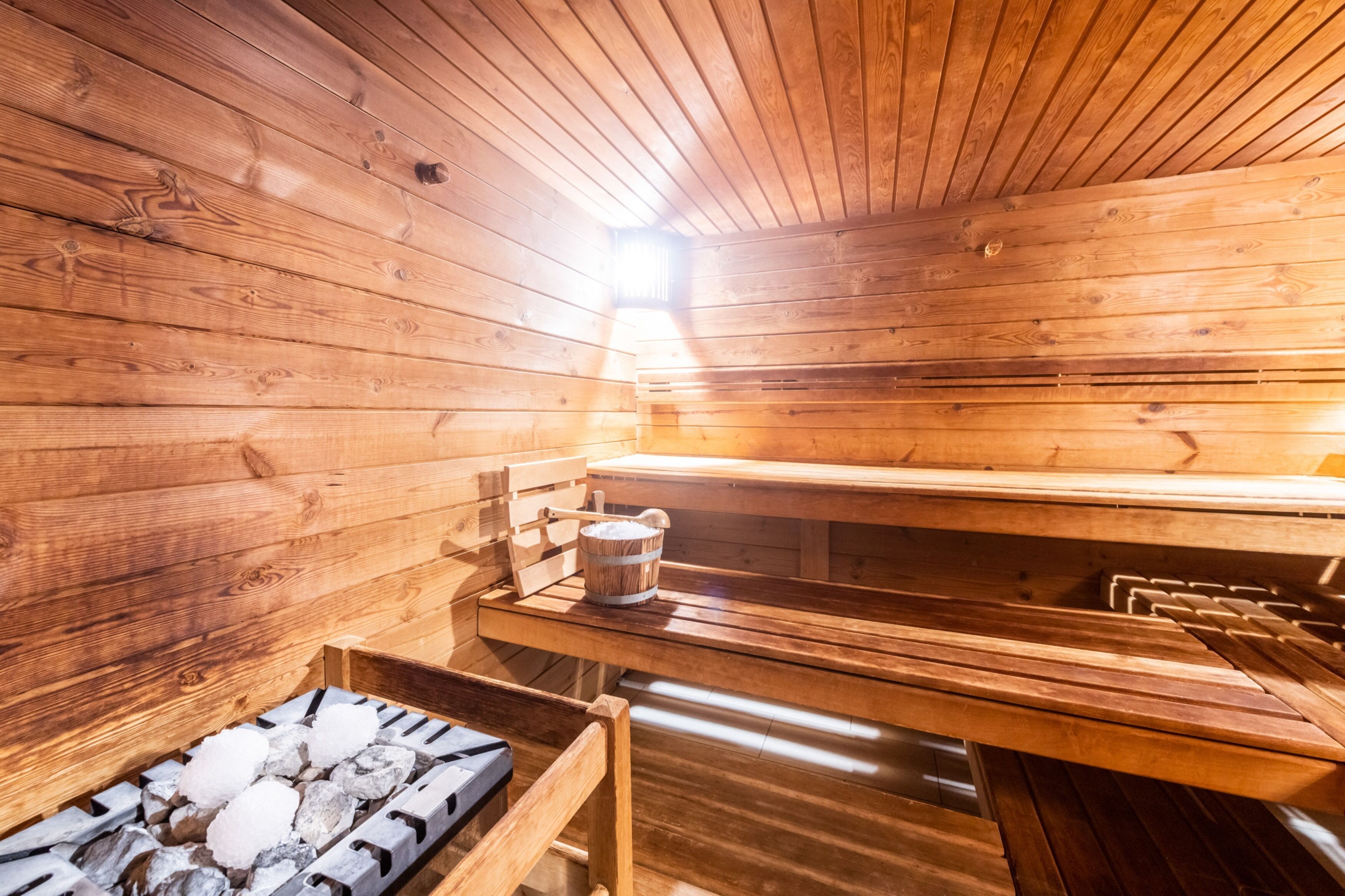 Una sauna con paredes y bancos de madera, un balde y una bandeja de hielo.