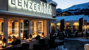 Un hotel llamado "LENZERHORN" con terraza exterior y vistas a montañas nevadas.
