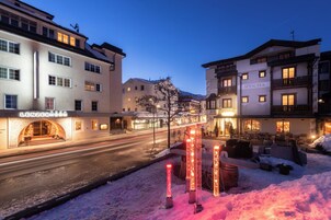 Un hotel con el suelo cubierto de nieve, señalización iluminada y una calle al fondo.