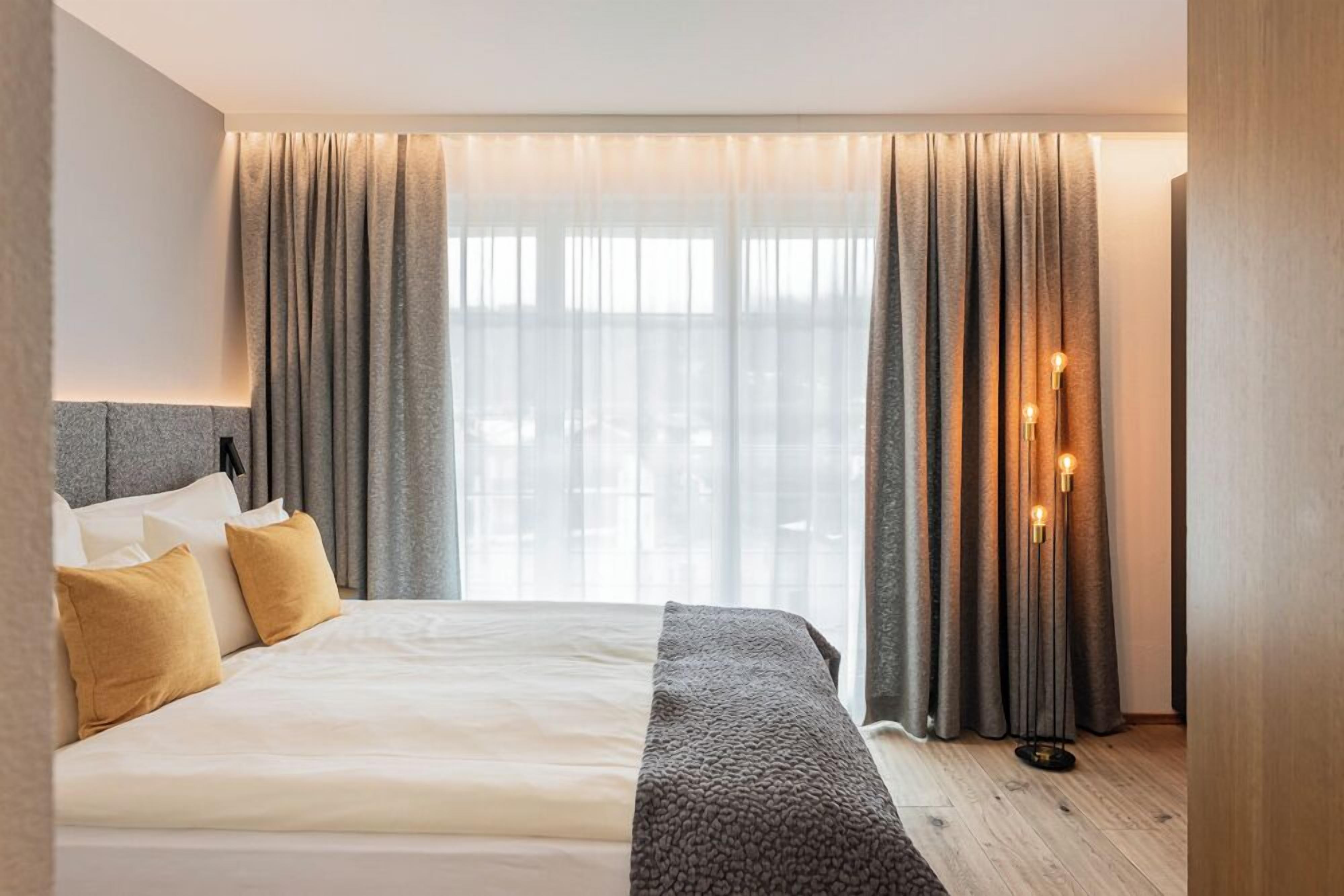 Habitación de hotel moderna con una cama grande, cortinas grises y una mesita de noche con una lámpara.