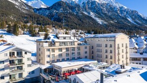 Un pueblo cubierto de nieve con edificios, incluyendo un hotel con balcones y un toldo rojo.