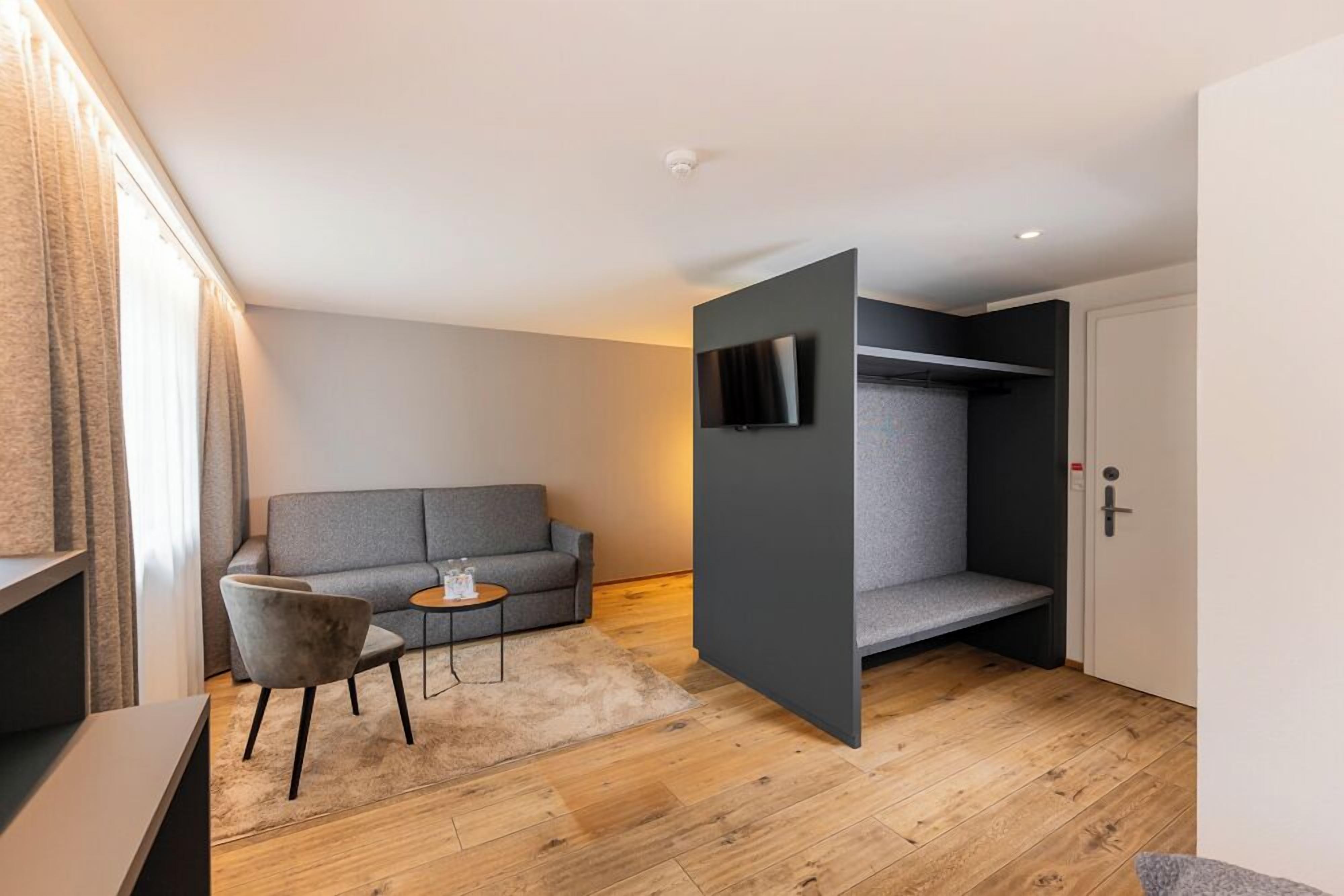 A modern room with a grey sofa, a small round table, and a TV mounted on a grey wall.