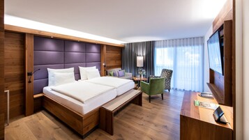 Habitación de hotel con una cama grande, un escritorio con silla, televisión y ventana con cortinas.