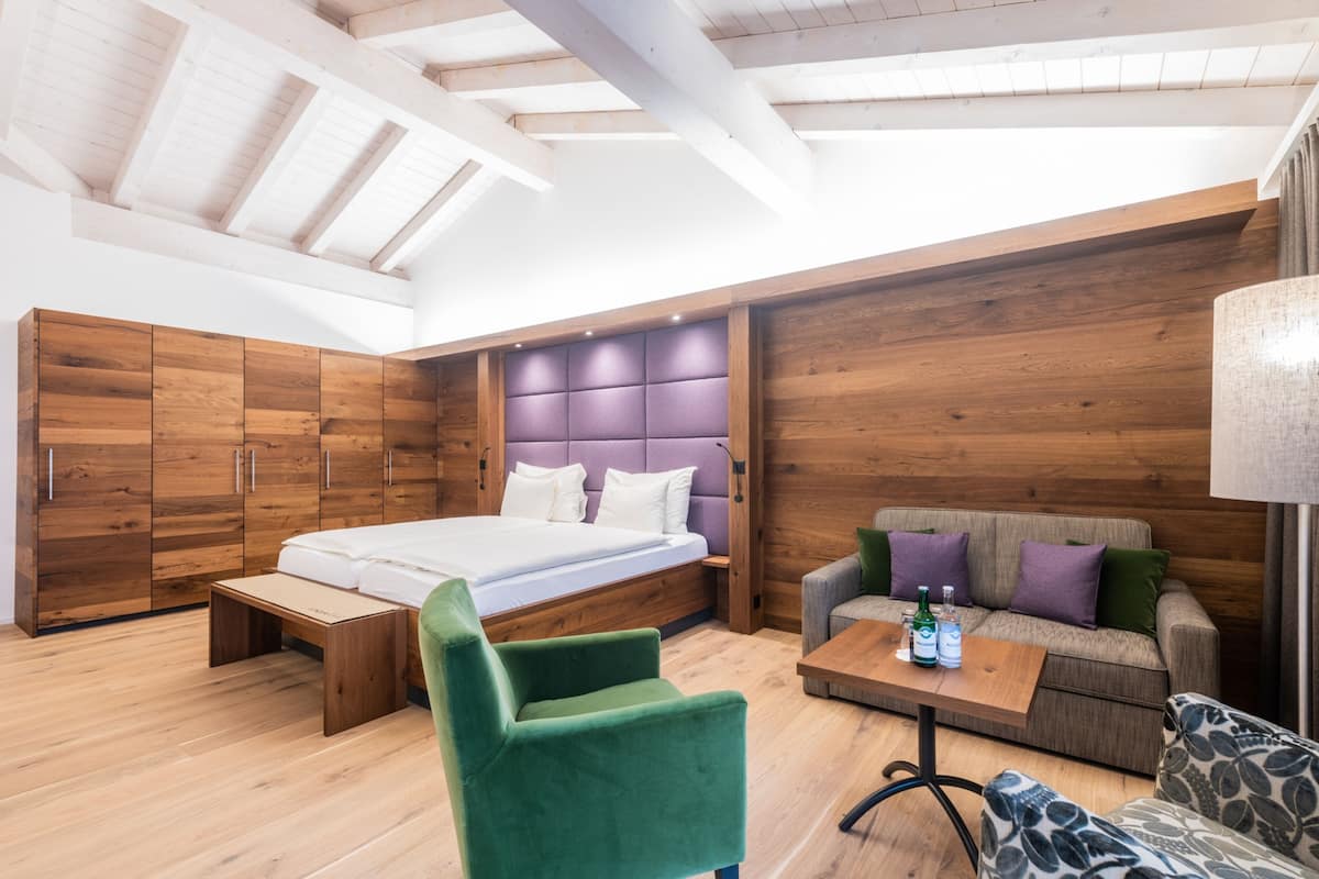 Un dormitorio moderno con techo estilo loft, una cama, un sillón verde, un sofá y una mesa de madera con botellas.