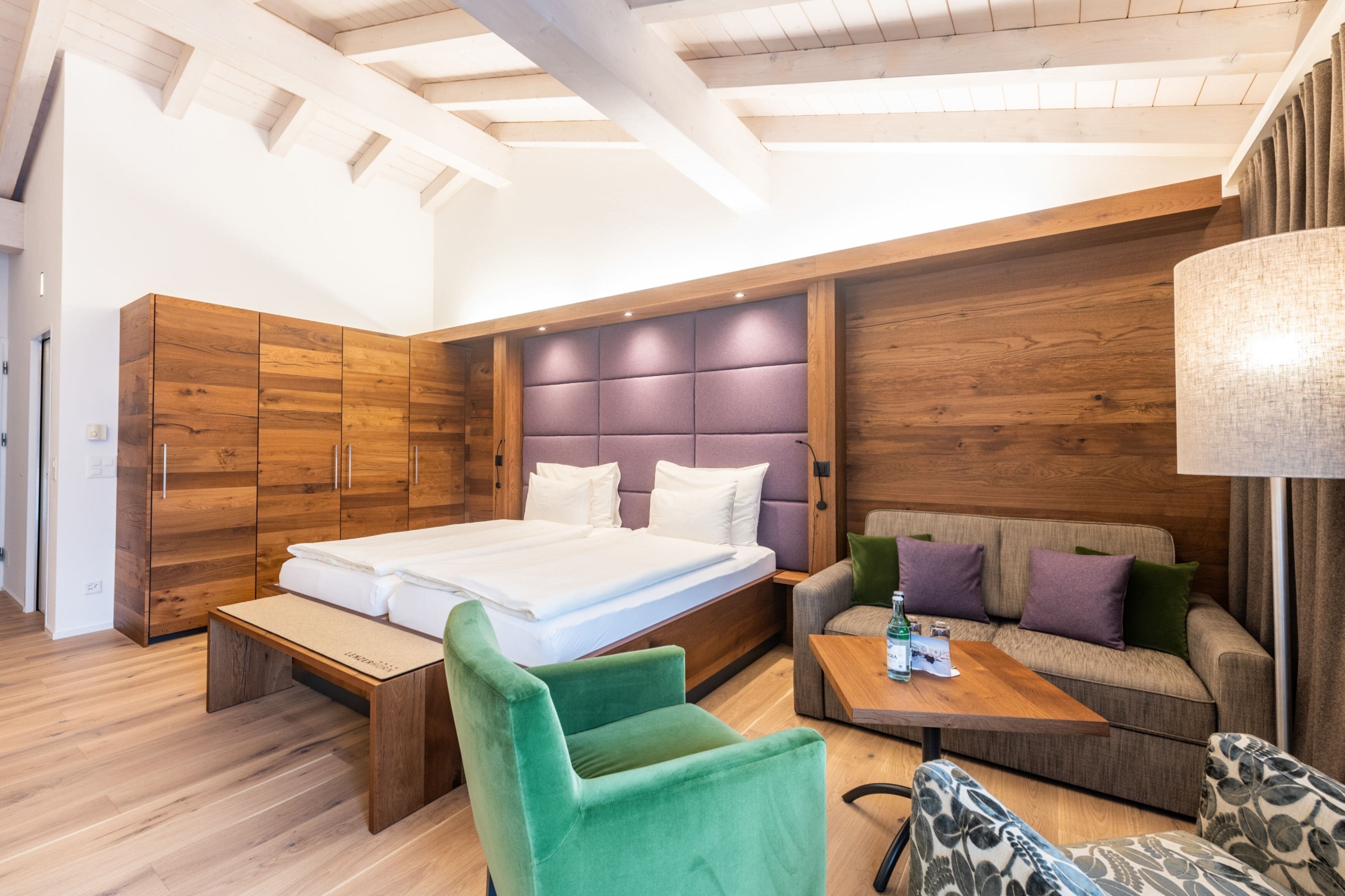 A modern bedroom with a large bed, wooden wardrobe, sofa, and a small table.