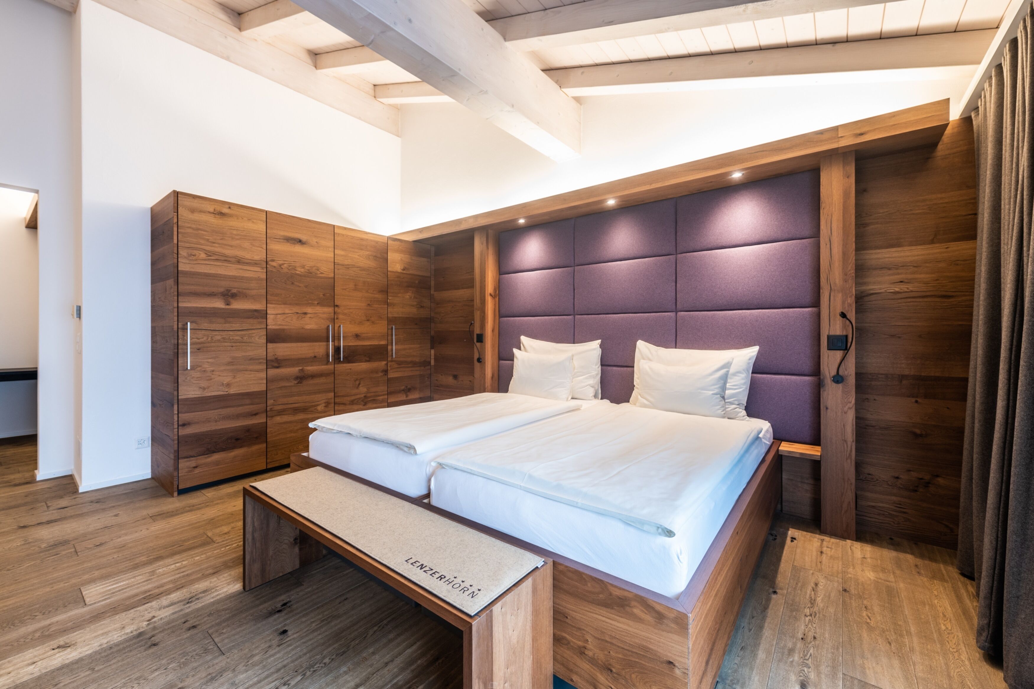 A modern bedroom with a wooden wardrobe, a bed with white linens, and a bench.