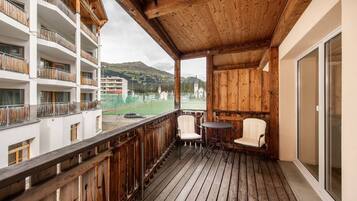 Ein Holzbalkon mit zwei Stühlen und einem Tisch, mit Blick auf ein Sportfeld und Gebäude.