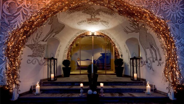 Una entrada imponente con un arco decorativo, un espejo que refleja el interior y una escalera que sube.