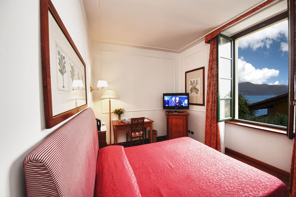 Een hotelkamer met een bed, een bureau met een stoel, een televisie en een raam met uitzicht op zee.