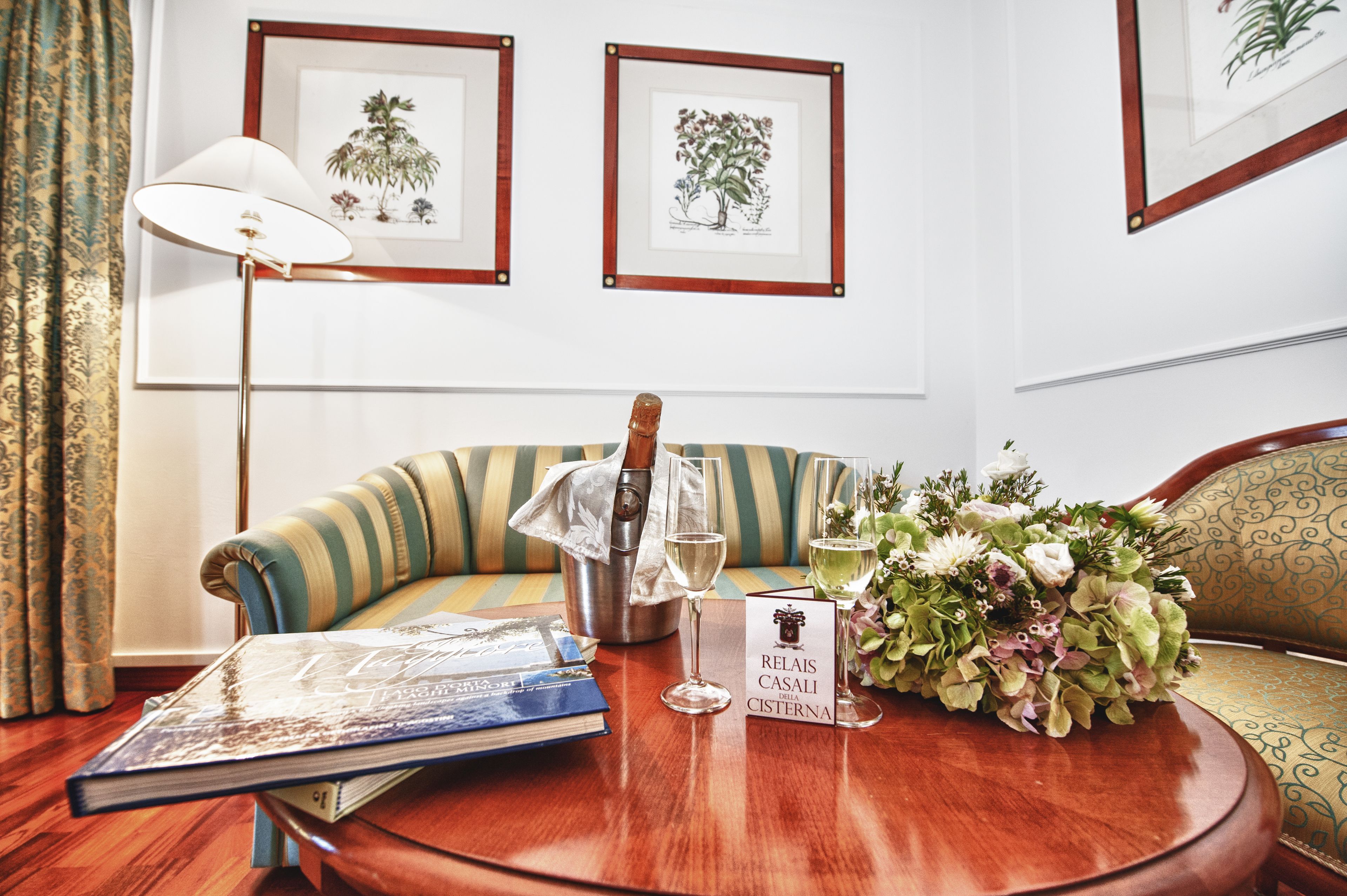 A room with a sofa, a table with a book, a wine glass, a bottle, and a bouquet of flowers.