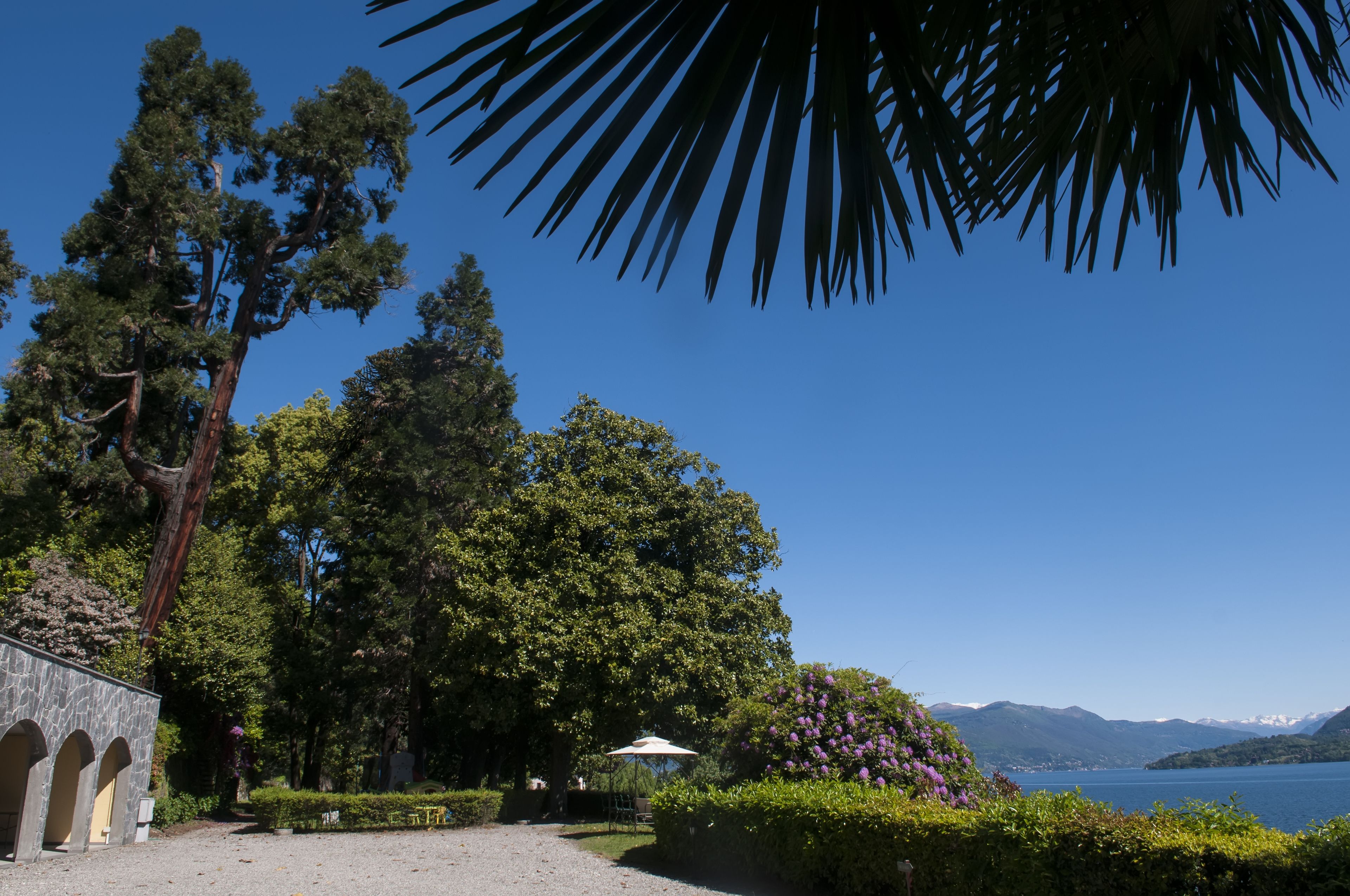 Ein friedlicher Seegarten mit einem Steinhaus, üppigem Grün und freiem Blick auf See und Berge.