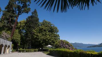 Ein friedlicher Seegarten mit einem Steinhaus, üppigem Grün und freiem Blick auf See und Berge.