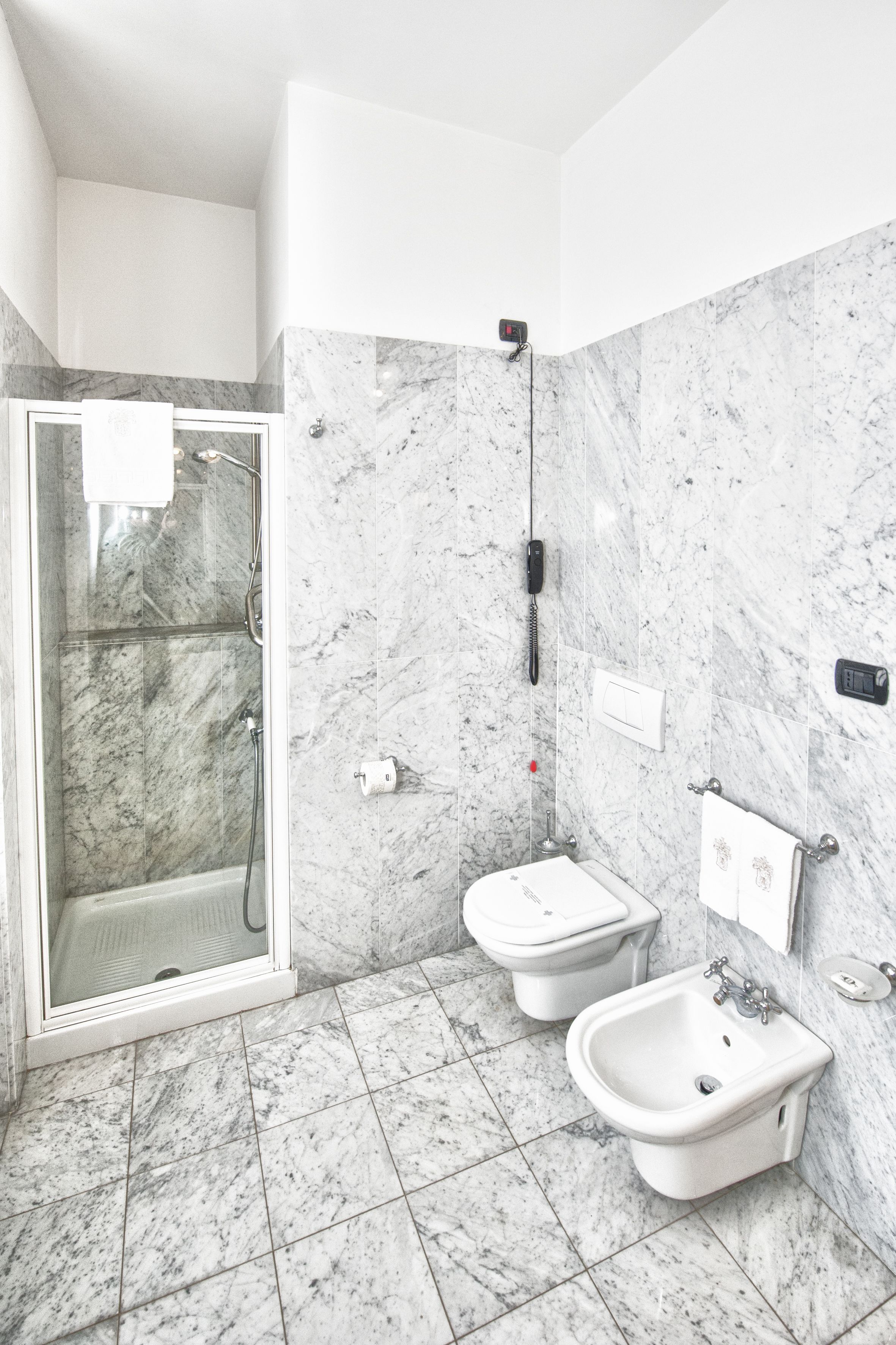 Een moderne badkamer met een glazen douchecabine, twee bidets en een marmeren vloer.