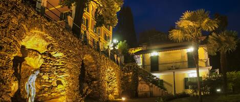 A stone wall with a statue, a building with balconies, and a well-lit pathway.