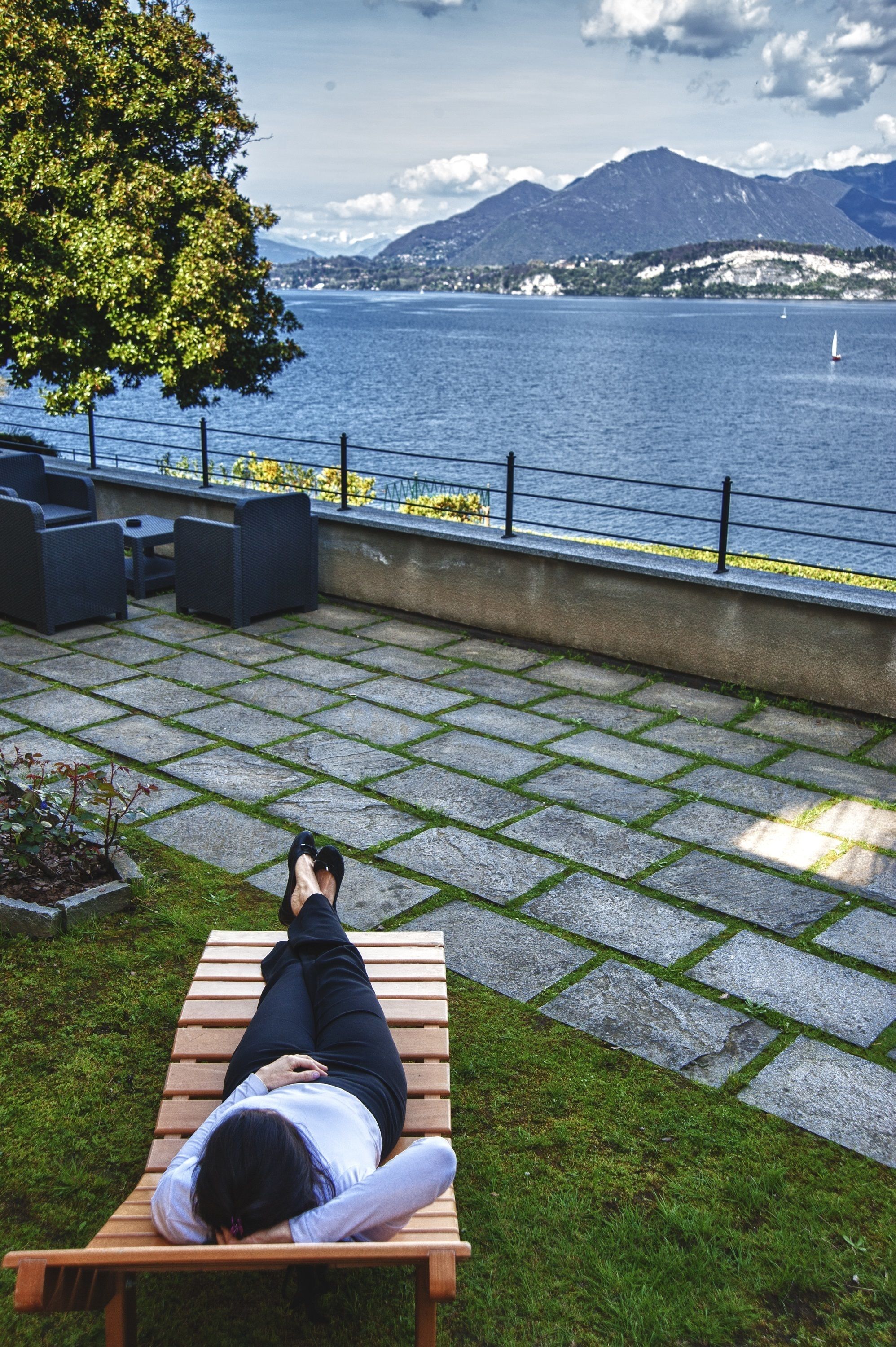 A person lying on a wooden bench overlooking a body of water with mountains in the background.