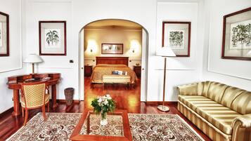Une chambre d’hôtel avec un lit, un canapé, un bureau et une chaise. Les murs sont ornés de tableaux encadrés et un vase de fleurs est posé sur la table.