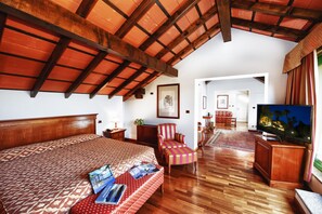 A spacious bedroom with a large bed, a wooden ceiling, a television, and a red-striped armchair. - Relais Casali della Cisterna (Belgirate)